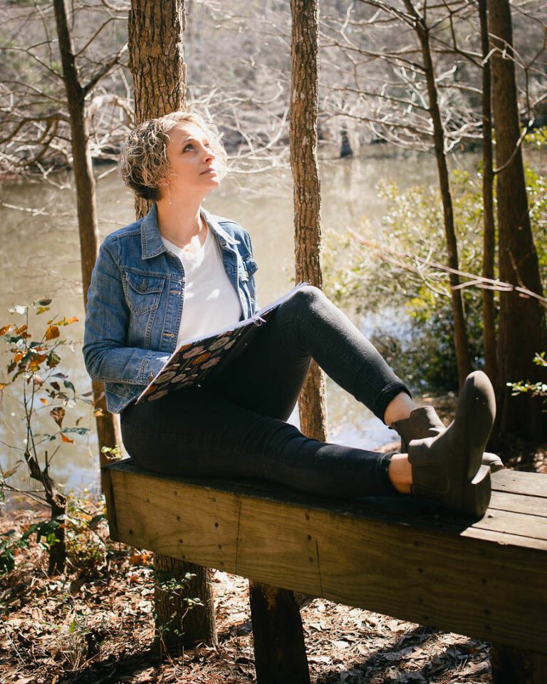 Woman sitting on park bench in the woods looking calm and happy improve your mental health Evoke Wellness Wilmington, North Carolina