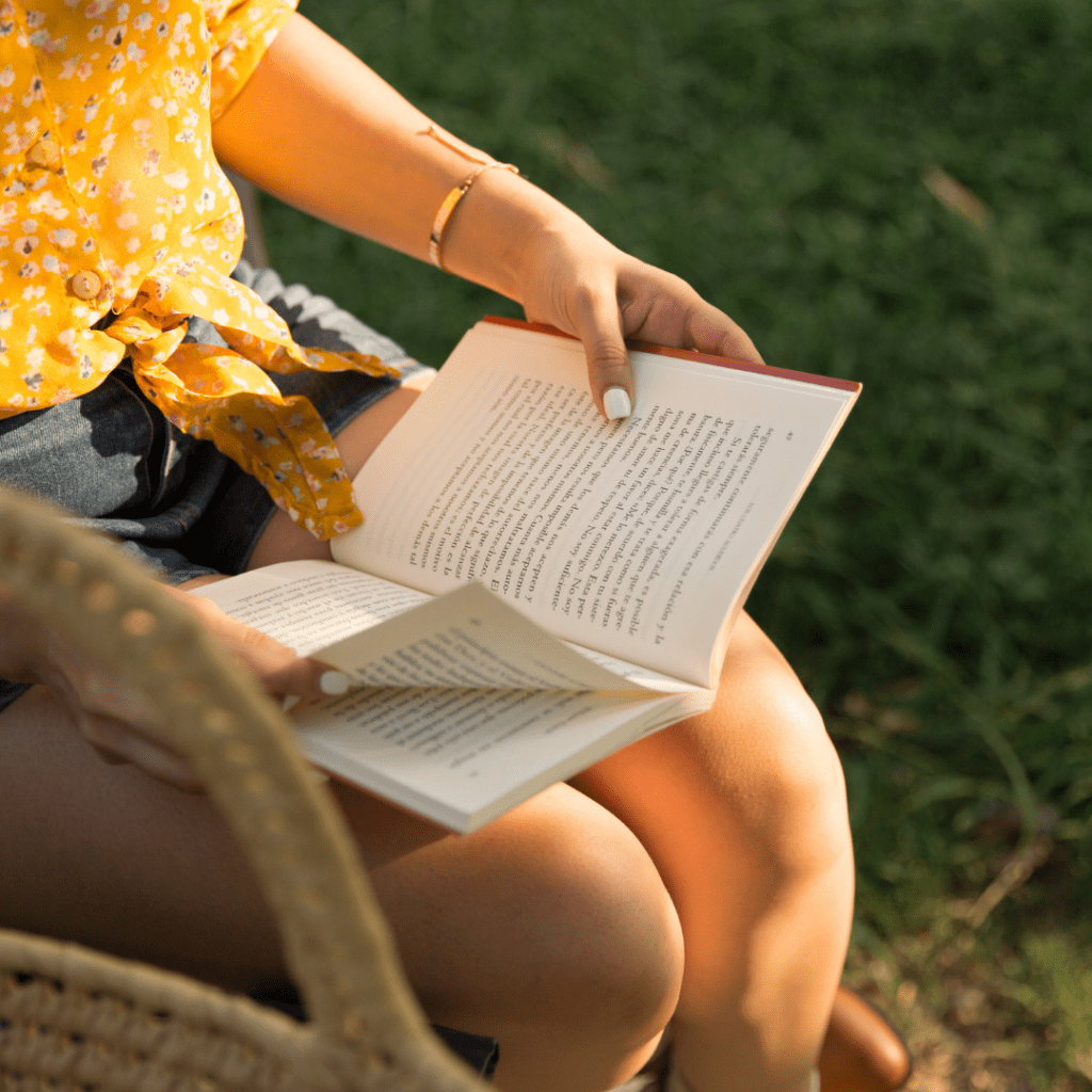 Woman in yellow shirt reading one of our team's favorite self-healing books The Four Agreements by don Miguel Ruiz Evoke Wellness Wilmington, North Carolina