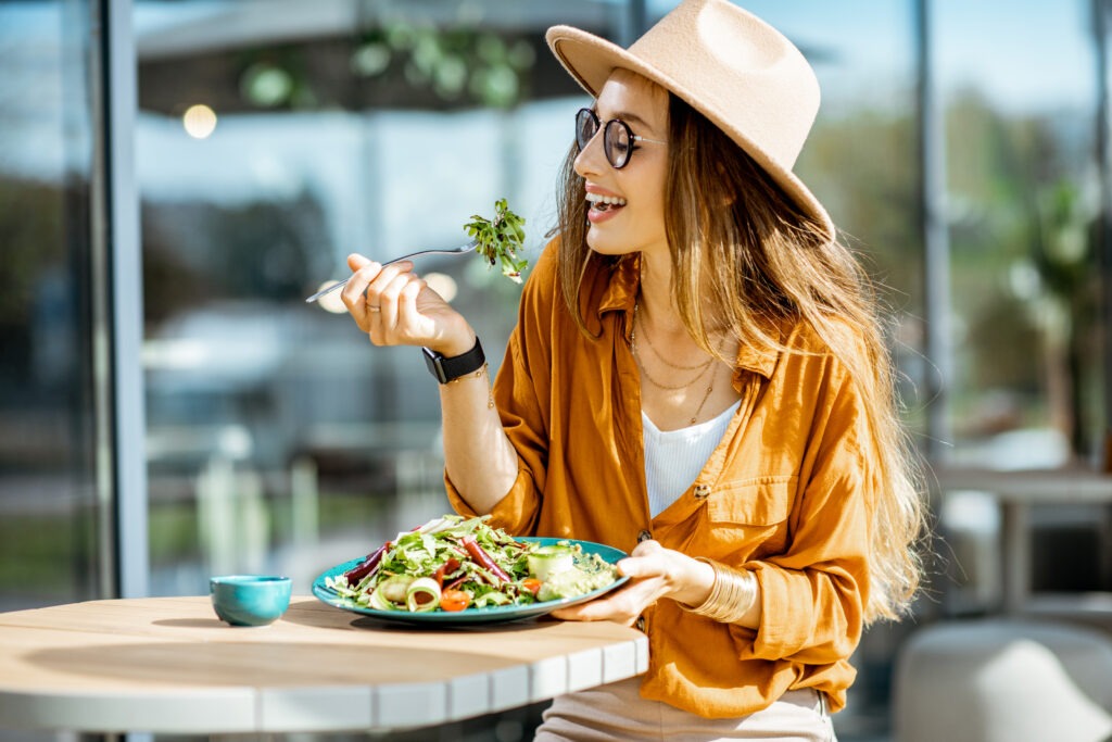 Woman in orange with hat and glasses eating a salad