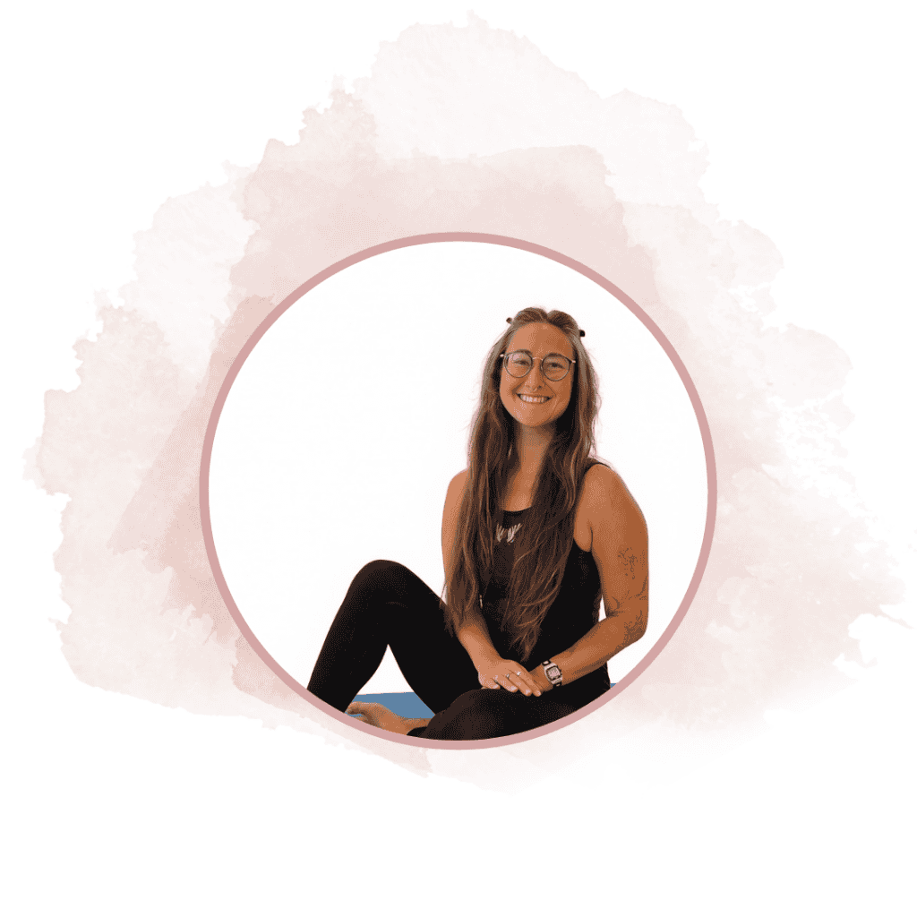 Profile portrait of a smiling woman with long hair and glasses, seated cross‑legged in a pink circular frame against a soft pink watercolor background.